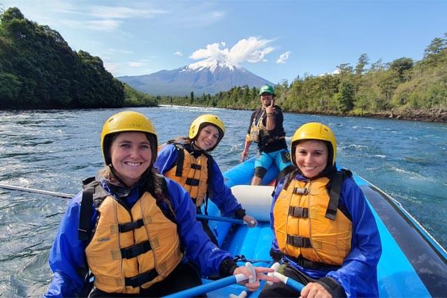 Grupo de aventureros en bote de rafting con el volcán Osorno de fondo, disfrutando de una experiencia única en el río Petrohué, Región de Los Lagos, Chile.