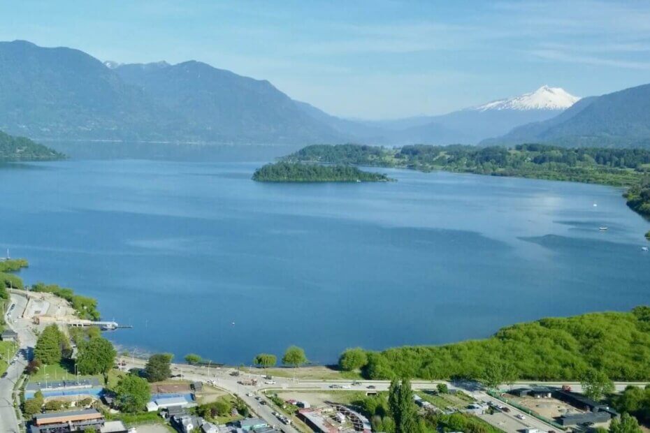 Vista aérea del Lago Panguipulli, con el volcán Mocho Choshuenco al fondo, rodeado de montañas y vegetación exuberante en la Región de Los Ríos, Chile.